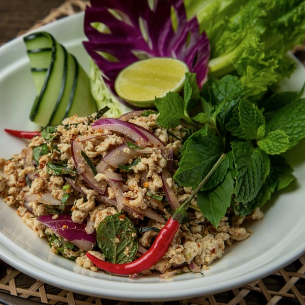 Close-up of a Thai Larb dish with minced chicken, red onions, mint, lime, and chili.