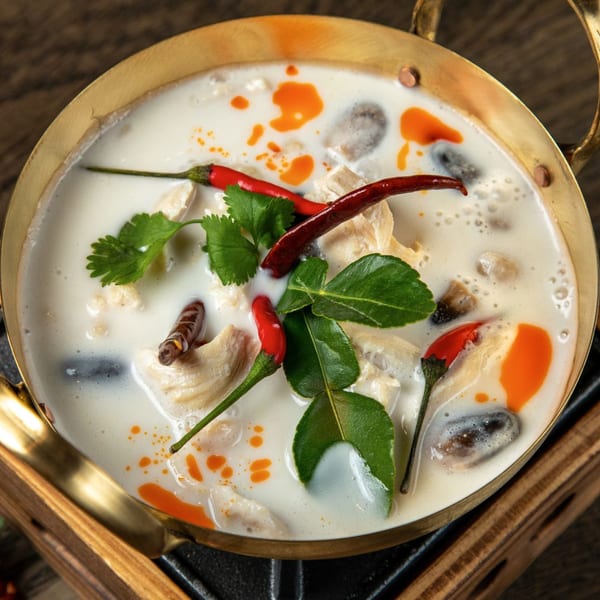 Close-up of Tom Kha Gai, a Thai coconut soup with chicken, mushrooms, chili, and lime leaves.