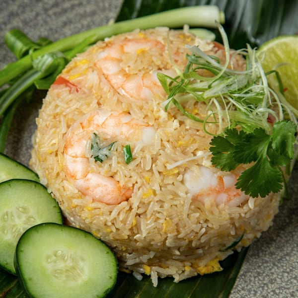 Shrimp fried rice with sliced cucumbers, green onions, and lime on a banana leaf.