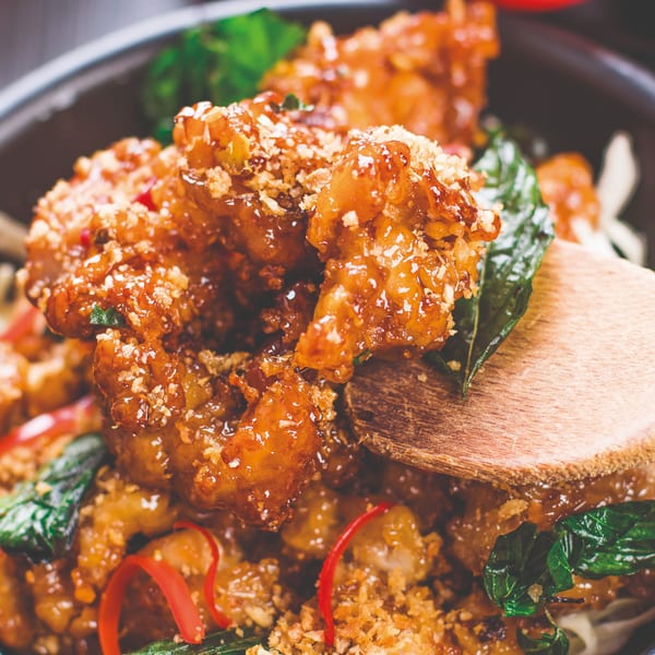 Close-up of crispy Thai chicken with sweet chili glaze, basil, and red pepper in a bowl.