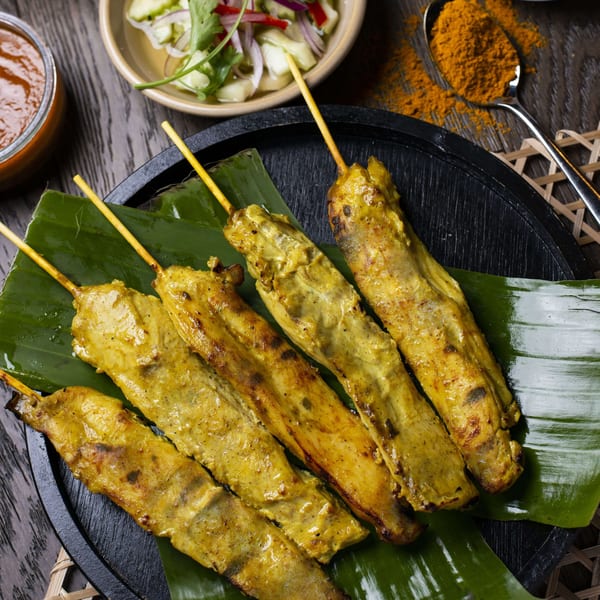 Grilled chicken satay skewers on banana leaves with dipping sauces and cucumber salad.