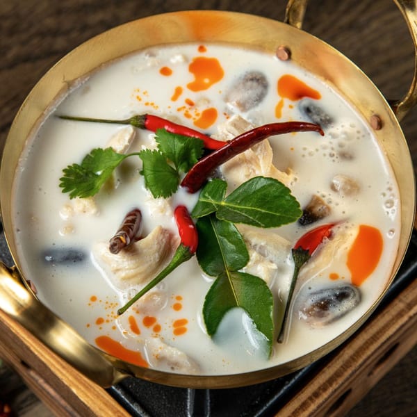 Close-up of Tom Kha Gai, a Thai coconut soup with chicken, mushrooms, chili, and lime leaves.